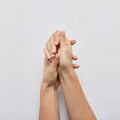 Two hands holding each other against a light gray background