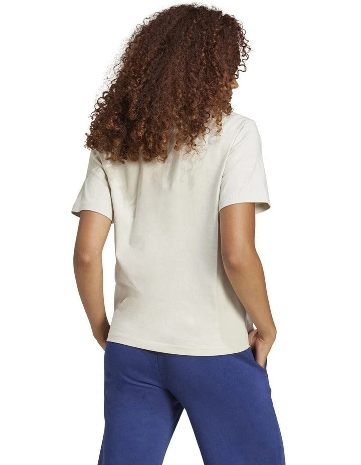 Person wearing a beige t-shirt with a logo and blue pants on a white background