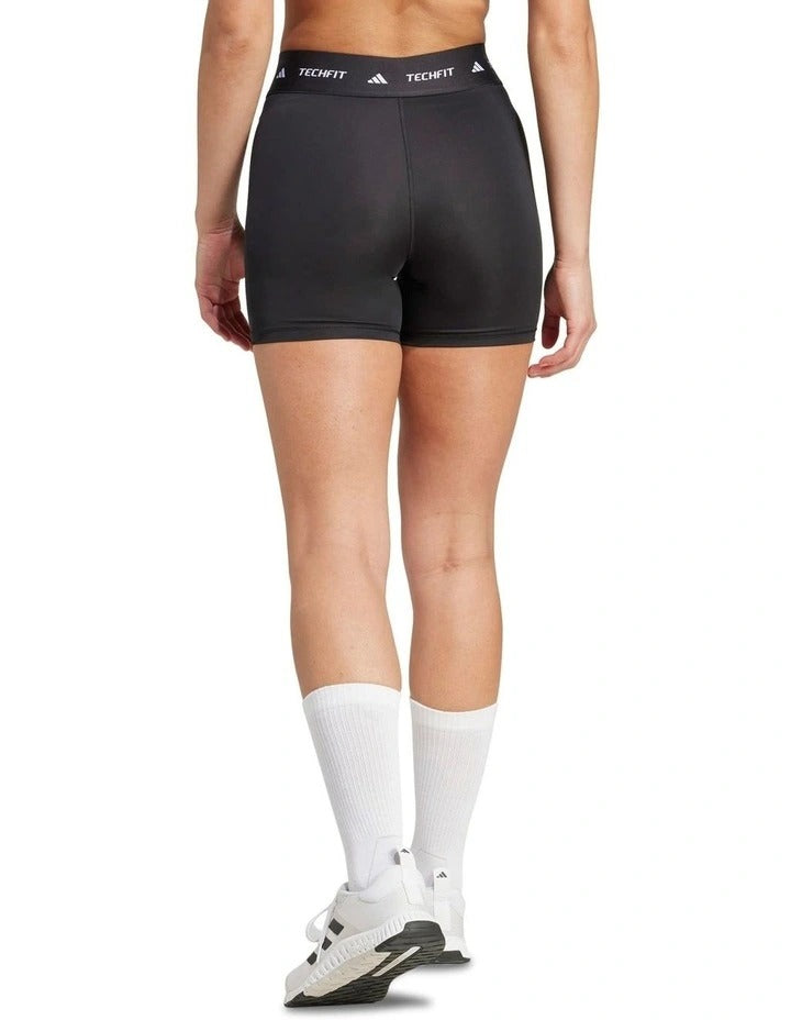 Person wearing black Adidas shorts and white socks holding a dumbbell on a white background